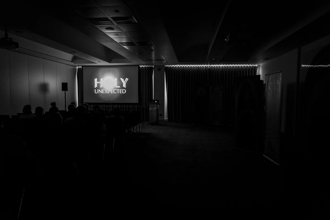 The Holy Unexpected film projected in a darkened screening area above seated viewers