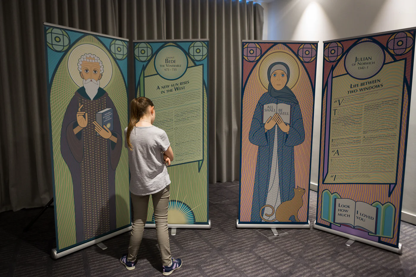 A visitor reading the paired Bede and Julian portrait and story panels